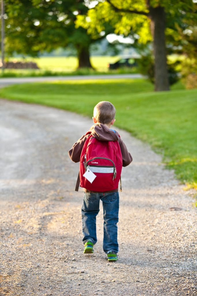 Boy walking down road with red backpack